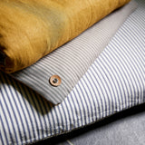 Close up of corner of Dog bed topper cushion folded back on floor cushion. Showing cotton ticking stripes and ochre linen.