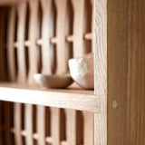 Close up of Shelve unit in ash wood. Three shelves. Woven wood back. Two ceramic dishes on shelf.