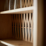 Close up of oak cabinet showing two oak shelves and woven wood back. Two glass vases on shelf.