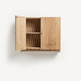 Oak cabinet with one door open and metal knobs. Shaker peg rail at bottom with black metal pegs. Door open showing woven wooden back.