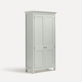 White painted freestanding tall cupboard Shaker style with panelled doors black metal knobs. Shown at an angle.