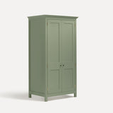 Green painted freestanding tall Armoire cupboard Shaker style with panelled doors and black metal knobs. Shown at angle with doors closed.