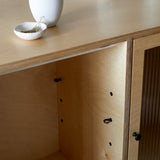 Close up of cabinet top edge with open door and closed reeded glass door. Simple white ceramic vase and dish on top.