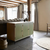 Three door ply wood contemporary side board with green painted doors, black metal knobs and feet shown in farmhouse room setting.