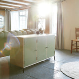 Three door ply wood contemporary side board with green painted doors, black metal knobs and feet shown in farmhouse room setting with bright sunlight from window.