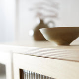 Top edge of ply wood cabinet showing ply lamination and reeded glass door with simple stoneware bowl and vase on top.