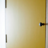 Yellow painted door with black metal door knob and hinges.