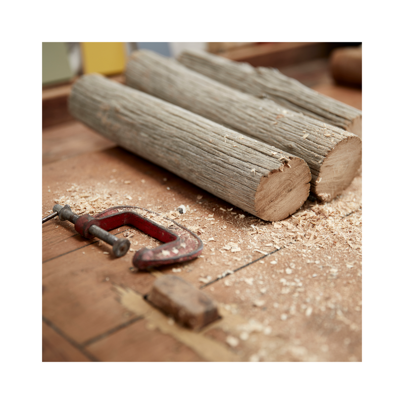 Two pieces of chestnut branch with red g clamp on work bench with saw dust.