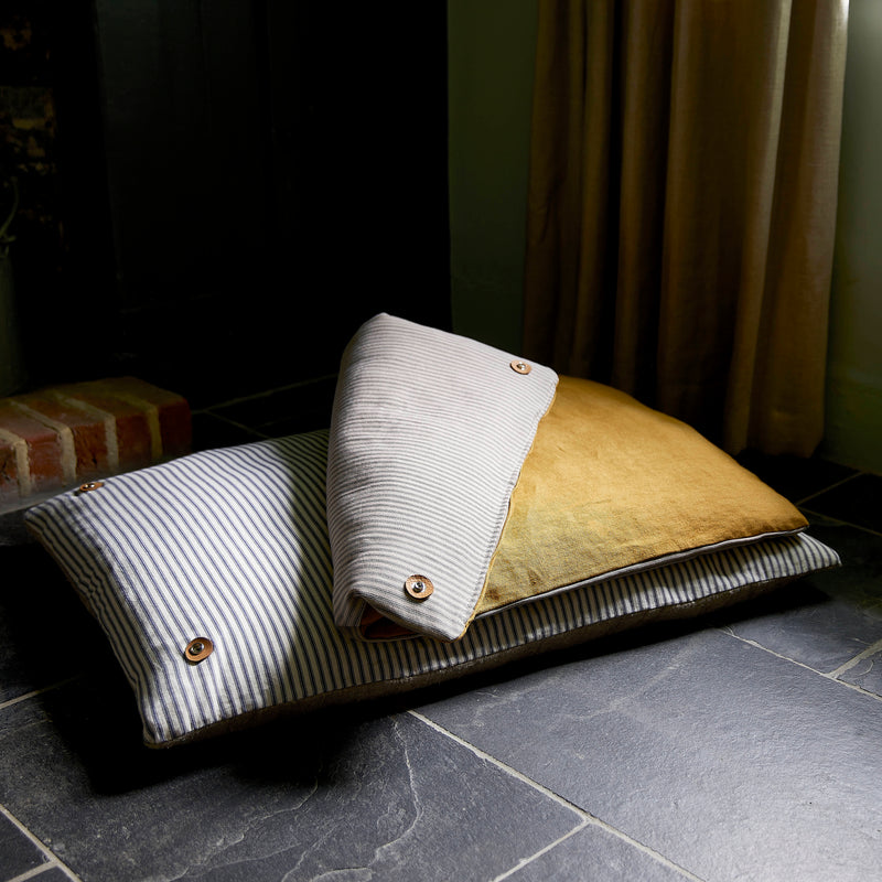 Dog bed topper cushion folded back on floor cushion. Showing cotton ticking stripes and ochre linen.