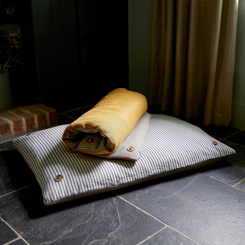 Dog bed topper cushion rolled up on floor cushion. Showing cotton ticking stripes and ochre linen.