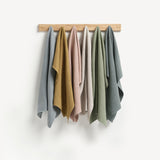 Six hanging lengths of linen fabrics. From left light blue, ochre, pink, oatmeal, green, blue