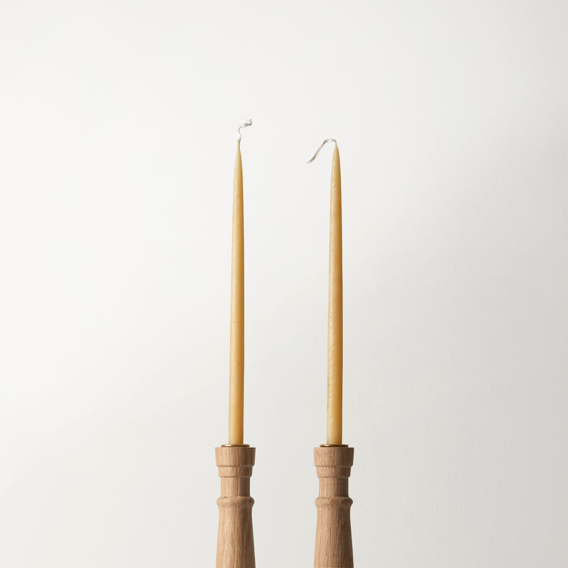 Two tall, thin candles in wooden holders on a light gray background