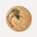 Round oak wood chopping board with pine needles on it