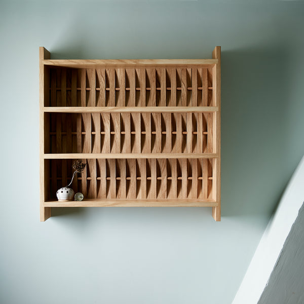 Shelve unit in oak wood. Three shelves. Woven wood back. Pictured on wall in blue room. Two small ceramic dishes on shelf.