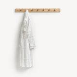 Oak Shaker peg rail with seven black metal knobs and a white summer dress hanging