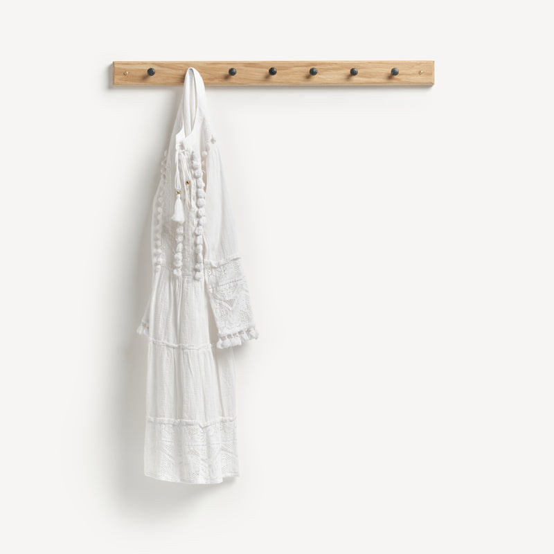 Oak Shaker peg rail with seven black metal knobs and a white summer dress hanging