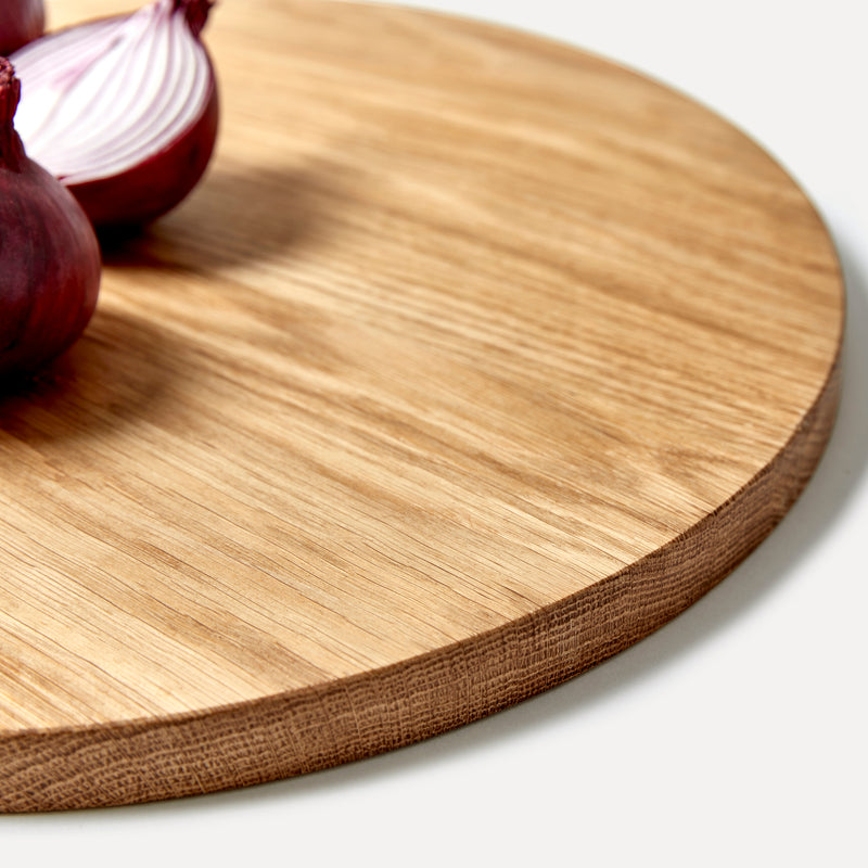 Round oak wood chopping board detail with red onions, one sliced