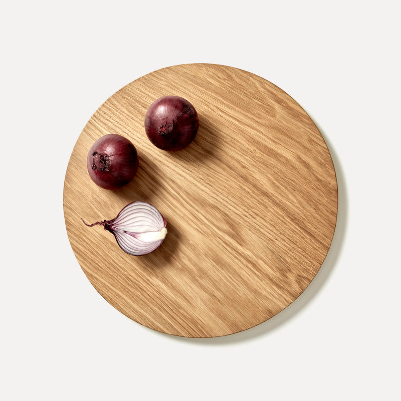 Round oak wood chopping board with red onions on it