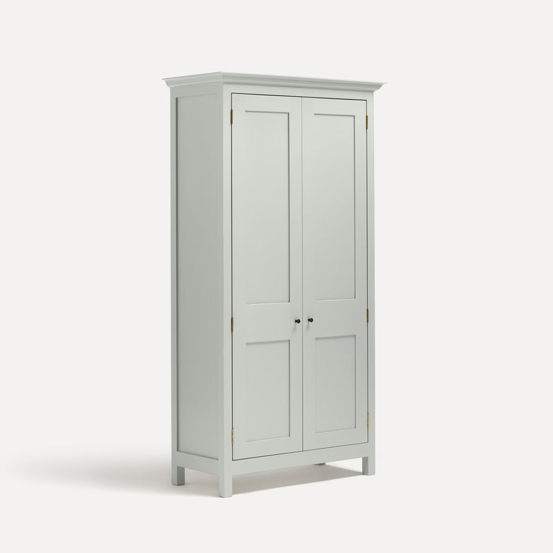 White painted freestanding tall cupboard Shaker style with panelled doors black metal knobs. Shown at an angle.