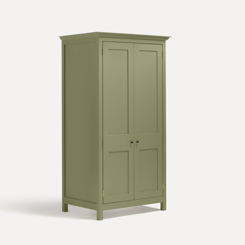 Green painted freestanding tall Armoire cupboard Shaker style with panelled doors and black metal knobs. Shown at angle with both doors closed.