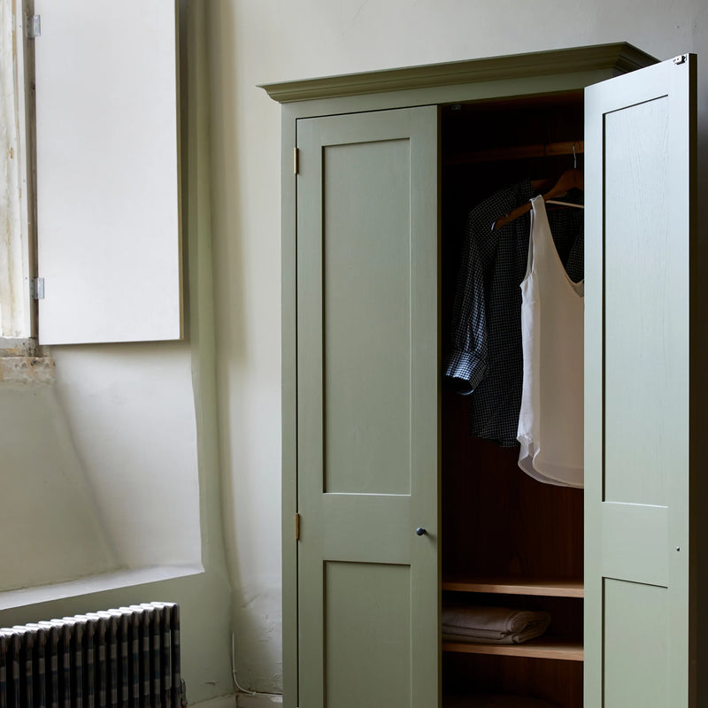 Armoire in room setting with one door open showing clothes on rail and on two shelves.