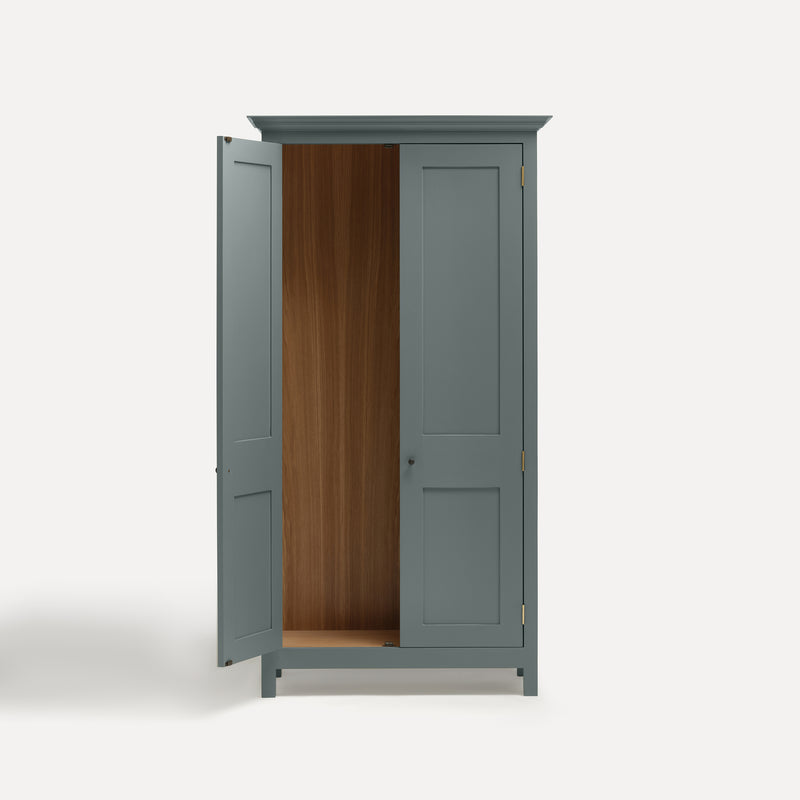 Blue painted freestanding tall Armoire cupboard Shaker style with panelled doors and black metal knobs. Shown face on with one door open.