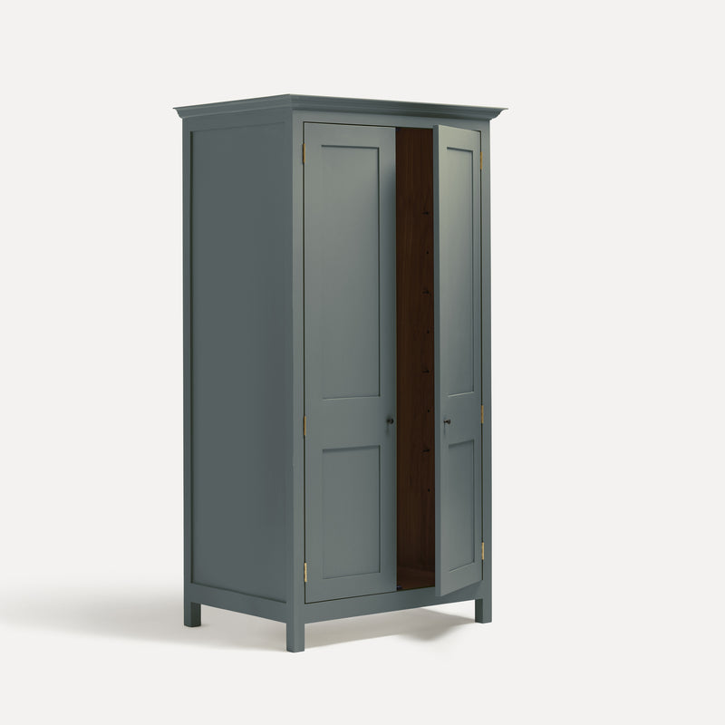 Blue painted freestanding tall Armoire cupboard Shaker style with panelled doors and black metal knobs. Shown at angle with one door open.