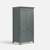 Blue painted freestanding tall Armoire cupboard Shaker style with panelled doors and black metal knobs. Shown at angle with both doors closed.