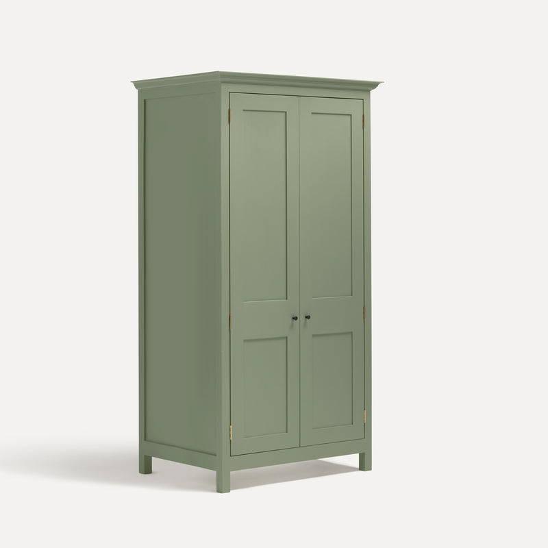 Green painted freestanding tall Armoire cupboard Shaker style with panelled doors and black metal knobs. Shown at angle with doors closed.