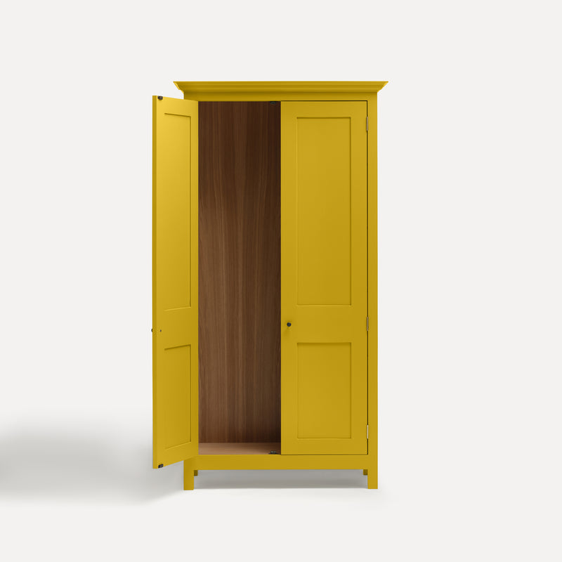 Yellow painted freestanding tall Armoire cupboard Shaker style with panelled doors and black metal knobs. Shown face on with one door open.
