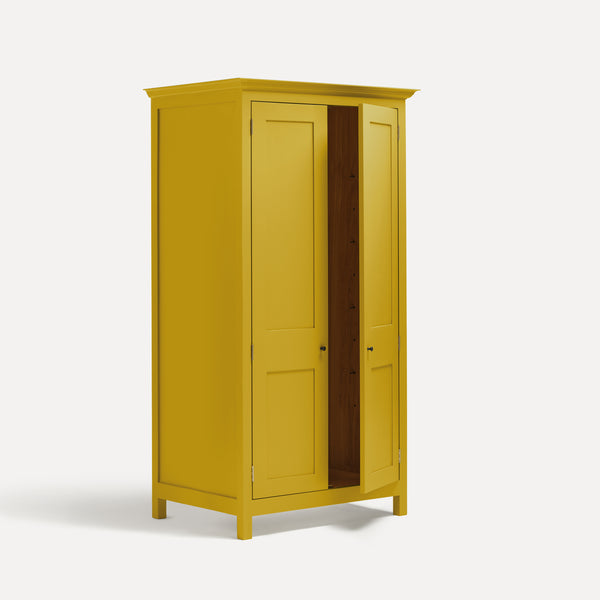 Yellow painted freestanding tall Armoire cupboard Shaker style with panelled doors and black metal knobs. Shown at angle with one door open.Yellow painted freestanding tall Armoire cupboard Shaker style with panelled doors and black metal knobs. Shown at angle with one door open.