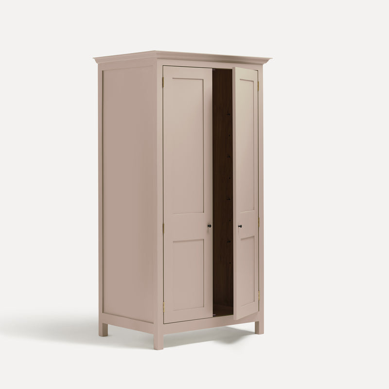 Pink painted freestanding tall Armoire cupboard Shaker style with panelled doors black metal knobs. Shown at angle with one door open.