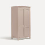 Pink painted freestanding tall Armoire cupboard Shaker style with panelled doors black metal knobs. Shown at angle with doors closed.