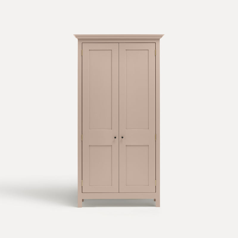 Pink painted freestanding tall Armoire cupboard Shaker style with panelled doors black metal knobs. Shown face on.