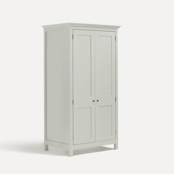 White painted freestanding tall Armoire cupboard Shaker style with panelled doors and black metal knobs. Shown at angle with doors closed.