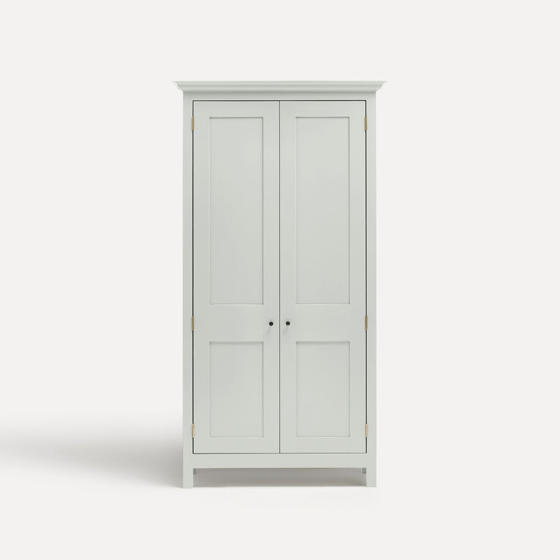 White painted freestanding tall Armoire cupboard Shaker style with panelled doors and black metal knobs. Shown face on with both doors closed.