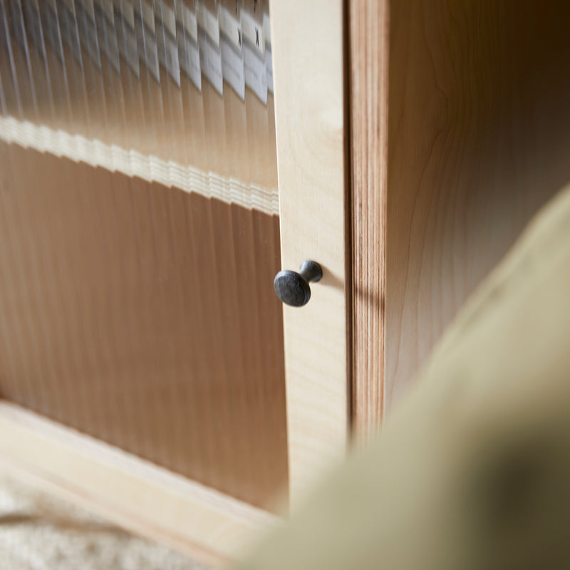 Close up showing edge of ply wood cabinet with reeded glass door and metal black door knob.