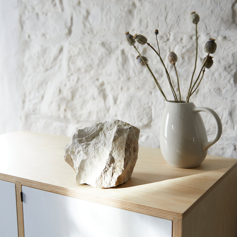 View down on top of contemporary plywood cabinet with painted white doors. White ceramic jug with dried poppy seed heads in and a large piece of natural chalk on top.