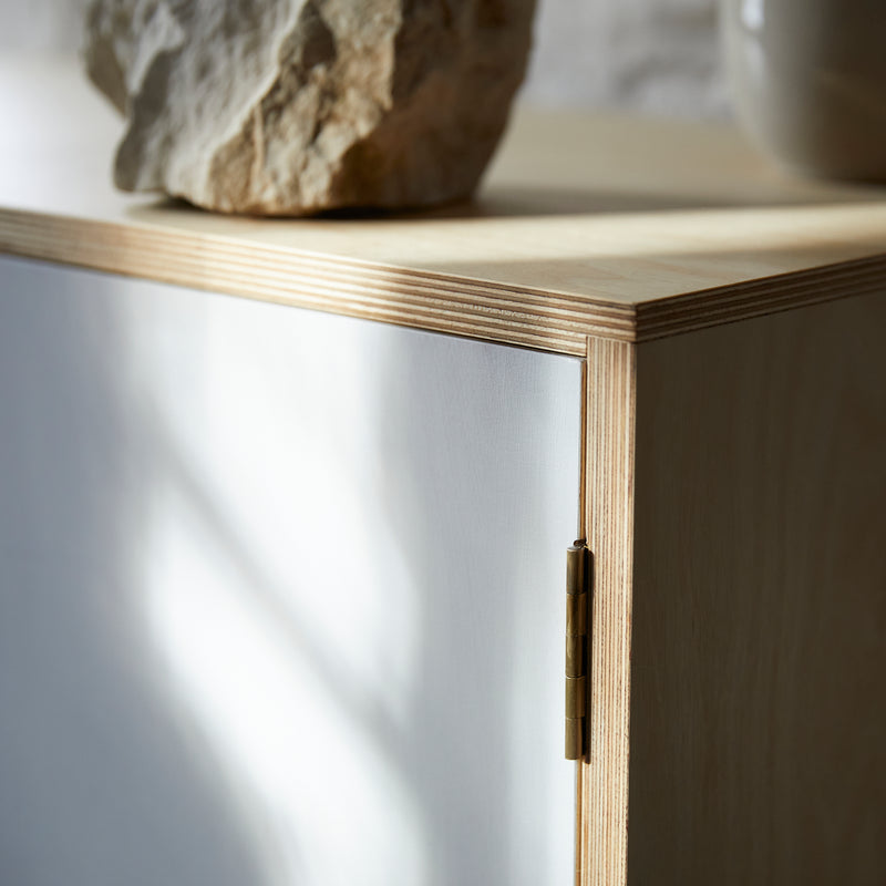 Close up of cabinet corner showing joint detail, ply laminations, hinge and white painted door. Out of focus large natural piece of chalk on top.