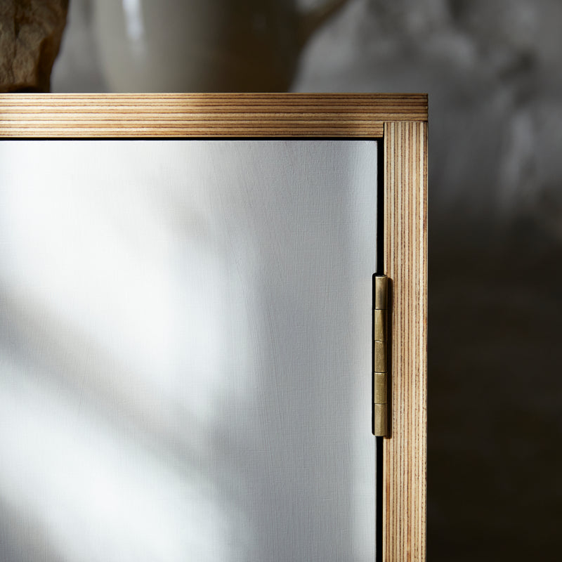 Face on close up of cabinet corner showing hinge, joint detail, ply lamination and white painted door.