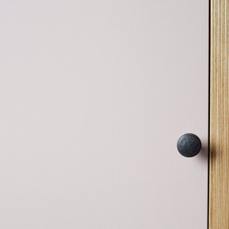 Face on close up of edge of sideboard showing ply wood lamination, pink painted door and black hammered door knob.
