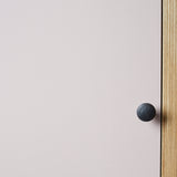 Close up of cabinet edge with vertical ply strip, pink painted door and black metal door knob.