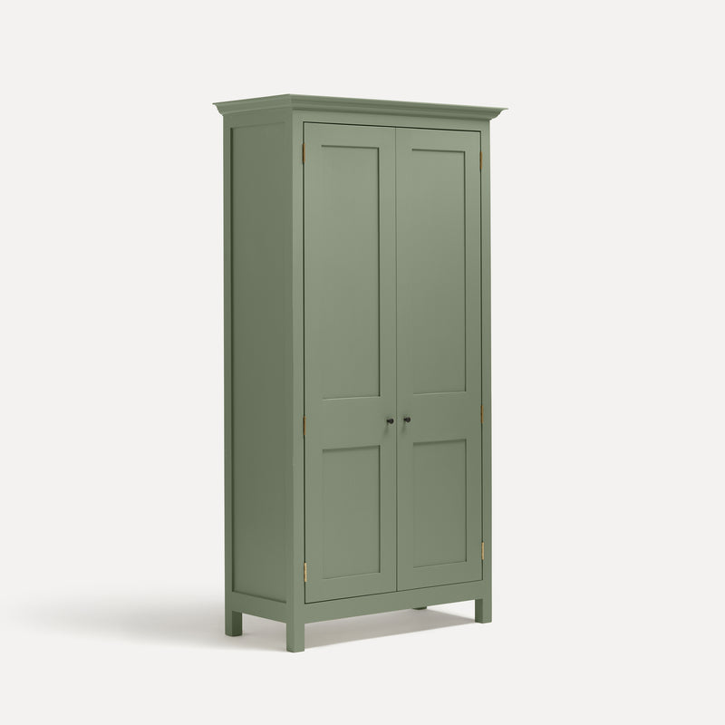 Green painted freestanding tall cupboard Shaker style with panelled doors black metal knobs. Shown at an angle.