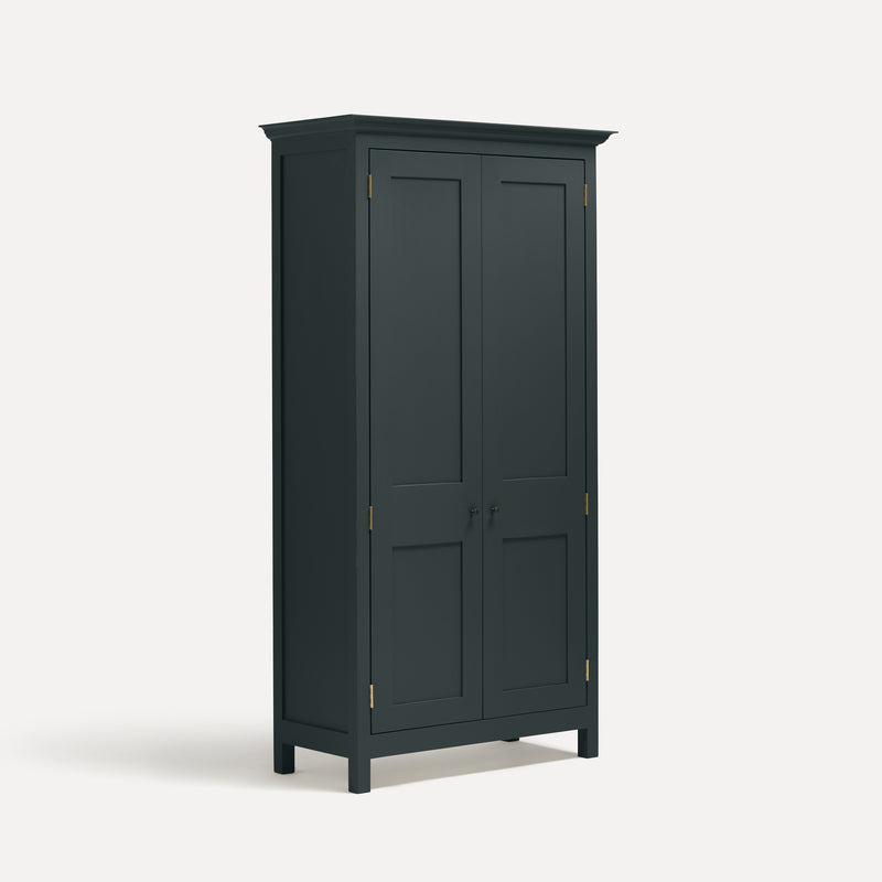 Dark grey blue painted freestanding tall cupboard Shaker style with panelled doors black metal knobs. Shown at an angle.