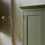 Close up of green painted shaker style cupboard showing cornice and brass hinges. Dried seed heads in foreground.