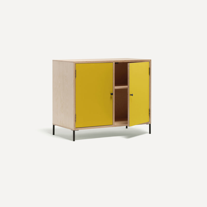 Two door ply wood contemporary side board with bold yellow painted doors (one open), black metal knobs and feet. Shown at an angle.