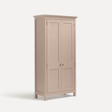 Pink painted freestanding tall cupboard Shaker style with panelled doors black metal knobs. Shown at an angle.