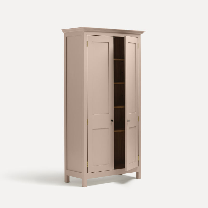 Pink painted freestanding tall cupboard Shaker style with panelled doors black metal knobs. Shown at an angle with one door open.