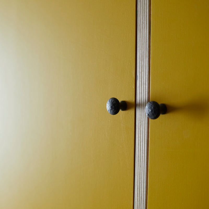 Close up of bright yellow painted doors with vertical ply wood divide and black metal door knobs.