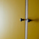 Close up of two bold yellow painted doors, vertical ply wood dividing them and two black metal door knobs.